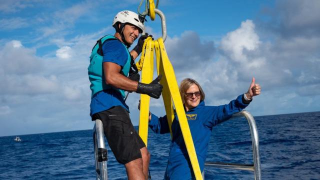 Dr Sullivan hanging from a winch over the ocean