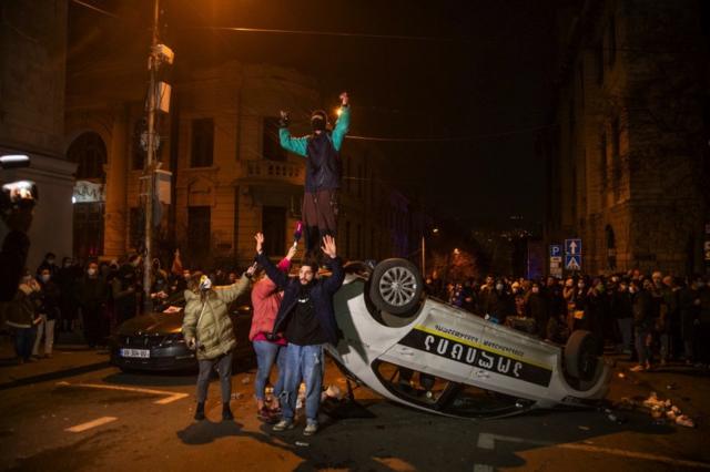 Участники протестов 8 марта стоят на перевернутой полицейской машины