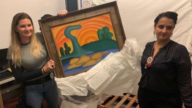 Policia Civil investigator and a delegate hold artist Tarsila do Amaral"s painting titled "Sol Poente" after it was seized during a police operation in Rio de Janeiro, Brazil