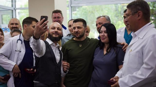 A handout photo made available by the Ukrainian Presidential Press Service shows Ukrainian President Volodymyr Zelensky (C) posing for a selfie with medical workers during a visit to a local hospital, in the Black Sea port city of Mykolaiv, southern Ukraine, 18 June 2022.
