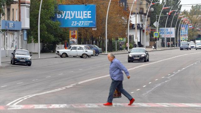 Мужчина на улице Мелитополя 26 сентября 2022 года. На заднем плане баннер с рекламой "референдума"