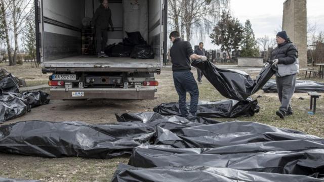 Мужчины собирают трупы в мешках в грузовик