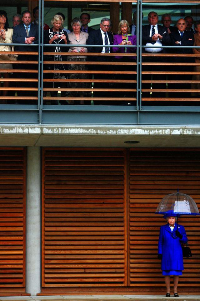 Queen Elizabeth II stands in the rain as guests take shelter at the opening of the Lawn Tennis Associations new headquarters in Roehampton, London, 2007