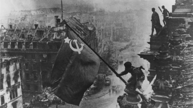 Russian soldiers flying the Red Flag over the ruins of the Reichstag in Berlin.