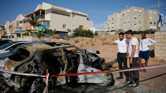 People look at a damaged car at a site where a rocket fired from Gaza landed, as Israeli-Palestinian cross-border violence continues, in Ashkelon, southern Israel, May 16, 2021