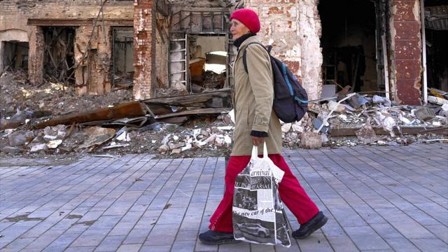 Женщина проходит мимо разрушенных зданий в Мариуполе