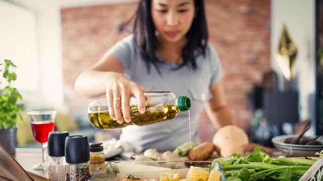 Une femme versant de l'huile d'olive sur une salade