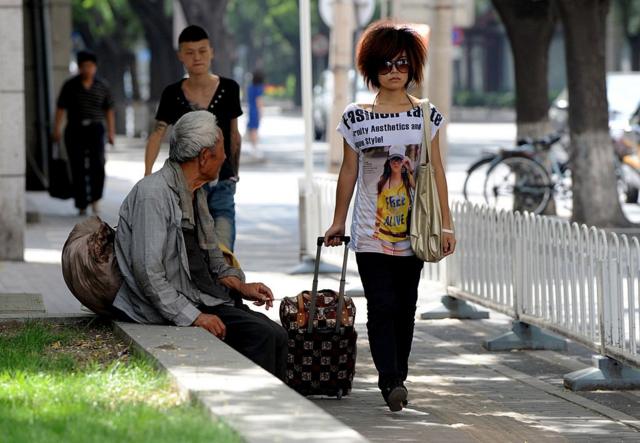 Нищий на улице Пекина, мимо него идет девушка с чемоданом