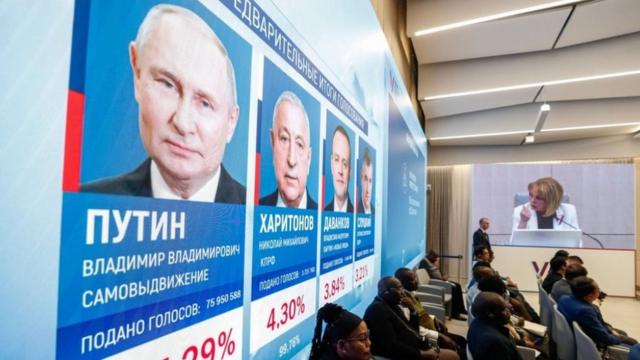 International observers sit in front of a screen showing preliminary results of the presidential elections at the Central Election Commission in Moscow, Russia