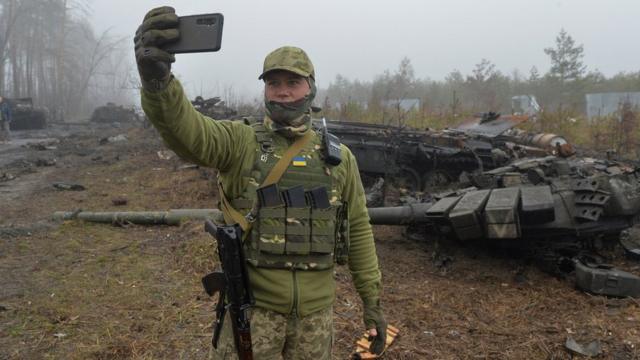 Украинский военный фотографируется на фоне разбитого российского танка