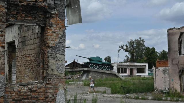 Разрушенный дом в городе Тростянец Сумской области и танк Второй мировой войны на постаменте на зеднем плане