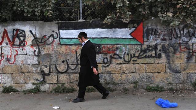 Еврейский ортодокс идет мимо палестинского флага