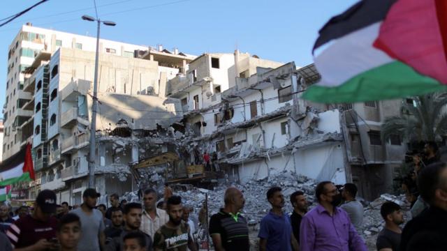 Palestinians hold a Palestinian flag and walk past a building destroyed by Israeli air strikes in the northern Gaza Strip as they take part in a protest at the Jerusalem Day flag march (15 June 2021)