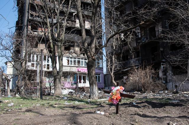 2022/03/26: A freshly dug grave next to two bombed out residential buildings in the besieged city of Mariupol.