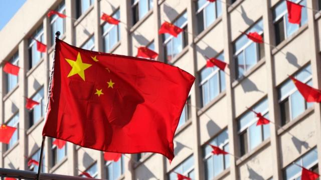 Флаг Китая на фоне здания, из окон которого также вывешены флаги Китая