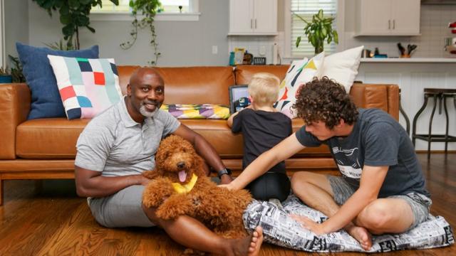 Peter, Anthony and Johnny sitting on the floor of their living room. A large brown dog is on Peter's lap.