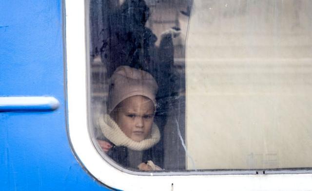 Дівчинка дивиться у вікно поїзда з жінками та дітьми, які втекли від бойових дій у Бучі та Ірпені. Поїзд рушав з міста Ірпінь до Києва, 4 березня 2022 року.