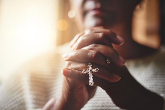 Une femme prie en tenant un chapelet avec une croix
