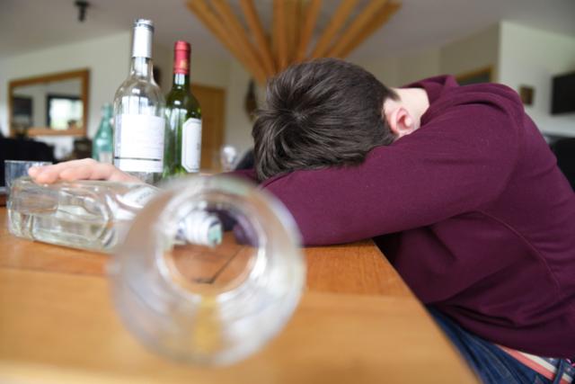Hình ảnh một thanh niên gục đầu trên bàn do say rượu, xung quanh là một số chai rượu