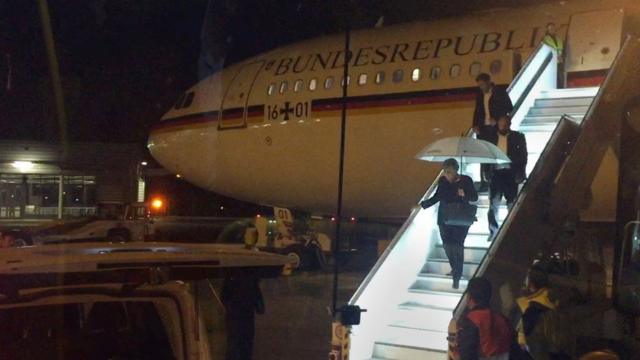 Ангела Меркель под зонтиком спускается с трапа самолета