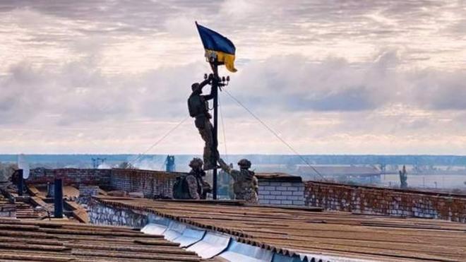 Солдат вешает украинский флаг на антенну на крыше