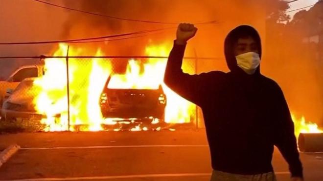 Протестующий на фоне горящей машины