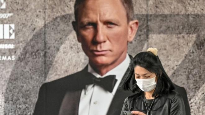 Woman in Thailand texts on her phone in front of a massive No Time To Die poster