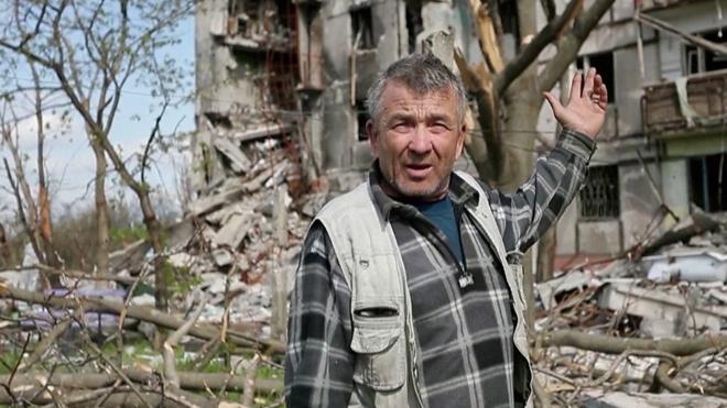 Сергей на фоне почти разрушенного дома в Мариуполе