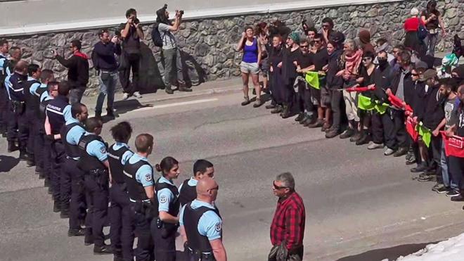 French gendarmes stand guard as demonstrators take part in a protest walk to help nearly 30 migrants to cross the Italian border to France at Montgenevre on April 22, during a weekend marked by action led by pro and anti-migrant groups. [Still image taken from Local Team video]