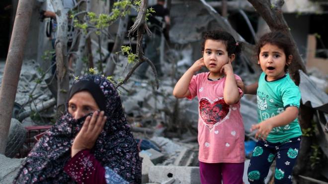 A Palestinian woman sits as two girls stand near destroyed houses in the northern Gaza Strip (1 June 2021)