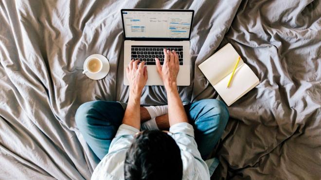 A man works on a laptop on his bed