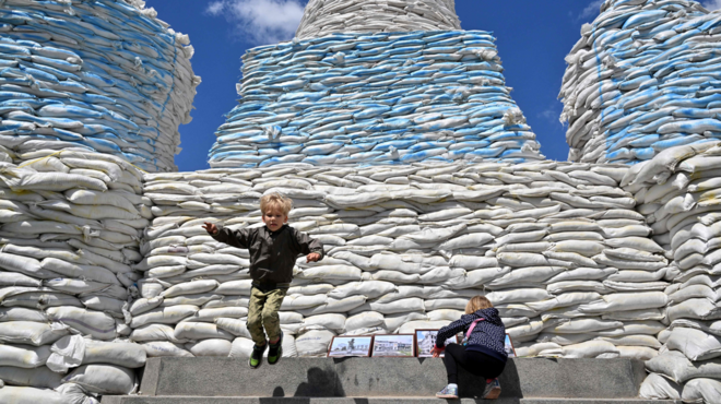 Children jumping and playing around a wall of sandbags