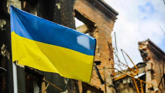 A Ukrainian national flag seen in front of destroyed buildings