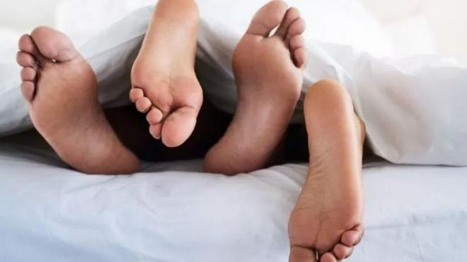 Des pieds d'un couple entrelacés sur un lit.