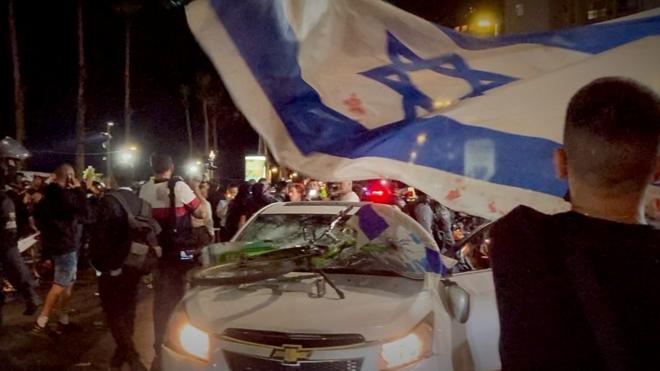 Парень с флагом Израиля напротив разбитой машины