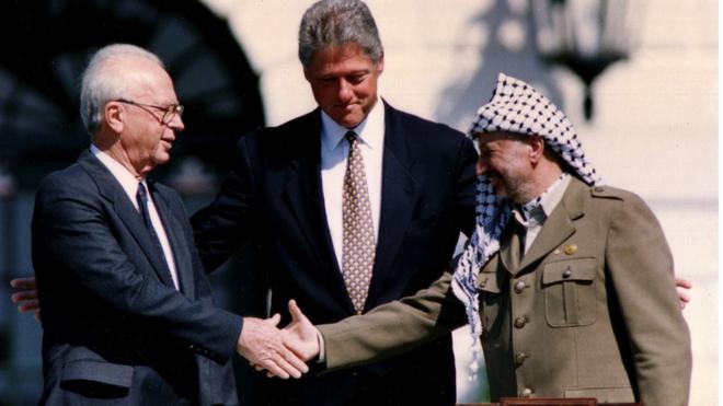 PLO Chairman Yasser Arafat (R) shakes hands with Israeli Prime Minister Yitzhak Rabin (L), as U.S. President Bill Clinton stands between them, after the signing of the Israeli-PLO peace accord, at the White House in Washington September 13, 1993