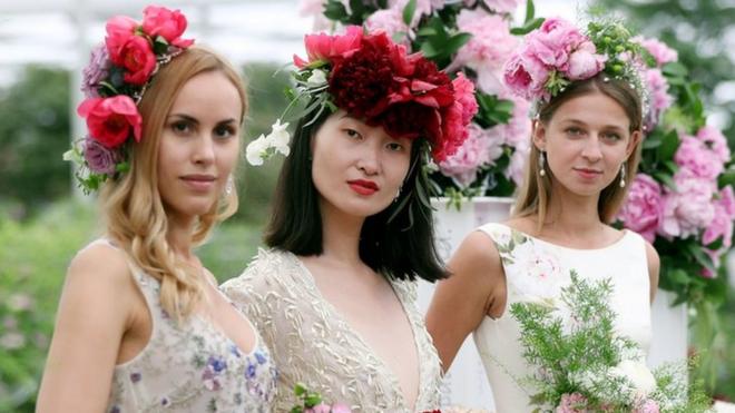 Three models wearing bridal designs by Alan Hannah hold bouquets of peonies in the Great Pavillion during the press day for this year's RHS Chelsea Flower Show