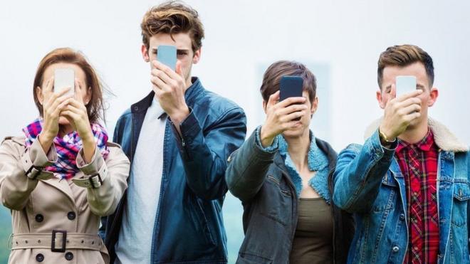 4 people holding their smartphones in front of their faces