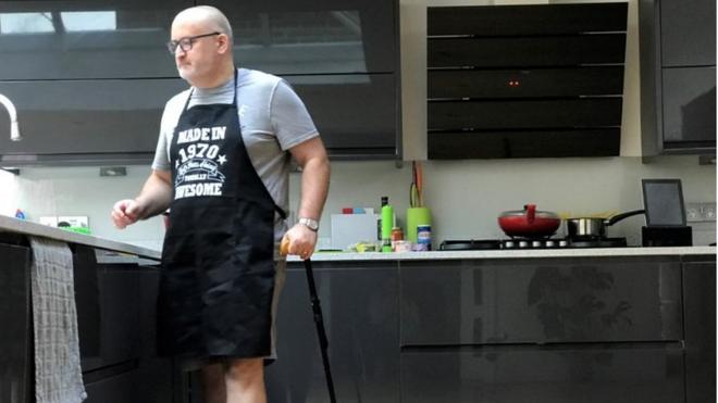 Ian Taverner standing in his kitchen with his walking stick