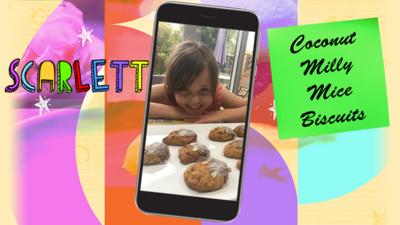 A little girl (Scarlett) smiling and crouching over a tray of coconut milly mouse biscuits.