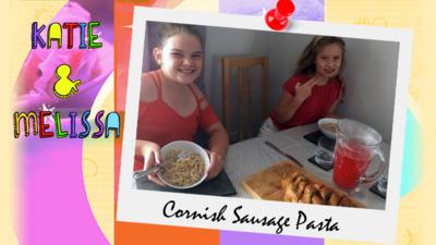 Two girls (Katie and Melissa) posing with a tableful of delicious food, including garlic bread, Cornish sausage pasta and raspberry lemonade.