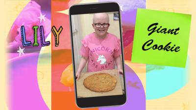 A little girl, called Lily, holds a huge cookie on a baking sheet.