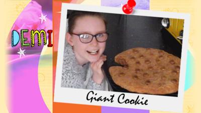 A girl posing with a giant chocolate chip cookie.