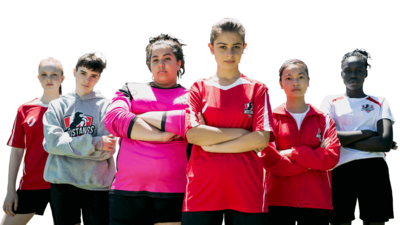 A group of six girls in football kits with their arms folded.