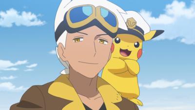 A young man with white hair is smiling whist a Pikachu with a captains hat sits on hi shoulder