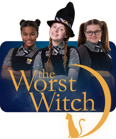Three young girls in school uniforms, capes and pointed witch hats all smiling to the camera. Above them is a sign that says "The Worst Witch"