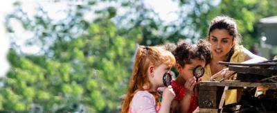 Two children looking at an insect through magnifying glasses with an adult looking on.