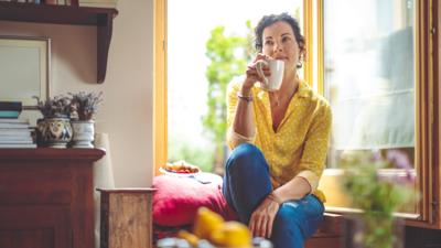 Woman sat having a coffee in her kitchen.