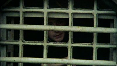 A young man looks through the bars of a prison
