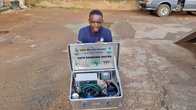 Timothy Kayondo squatting behind Eco Mobile Purifier